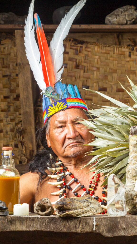 Un chamán amazónico anciano vistiendo un tocado de plumas tradicional y collares de cuentas en la comunidad de Wacaria.