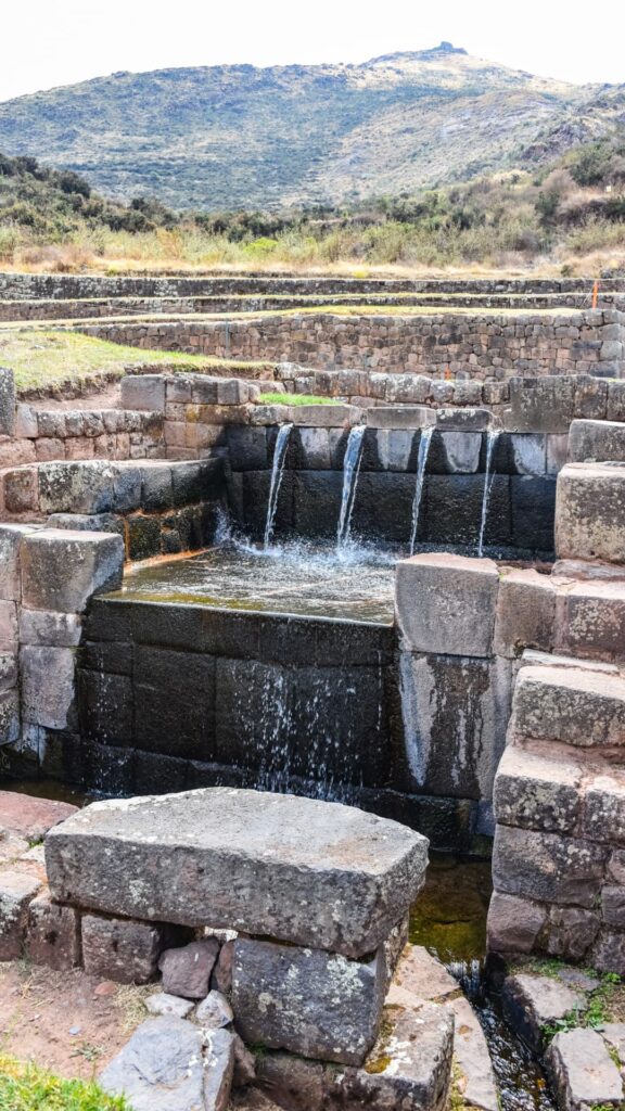Un primer plano de una fuente de agua de piedra tallada con agua fluyendo en el sitio inca de Tambomachay.