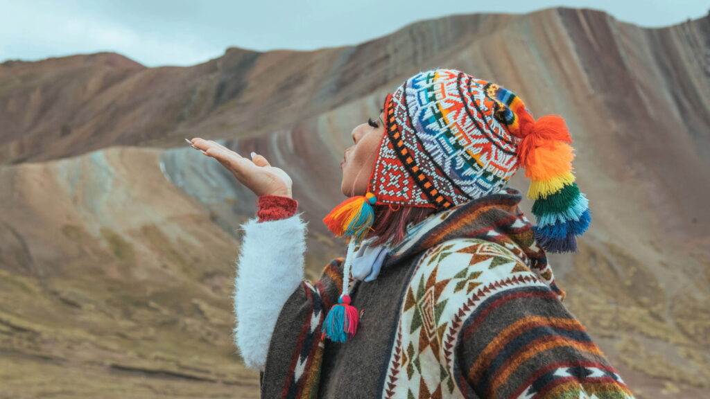 Un viajero que lleva un colorido chullo andino tradicional, lanzando un beso hacia la Montaña de Siete Colores.