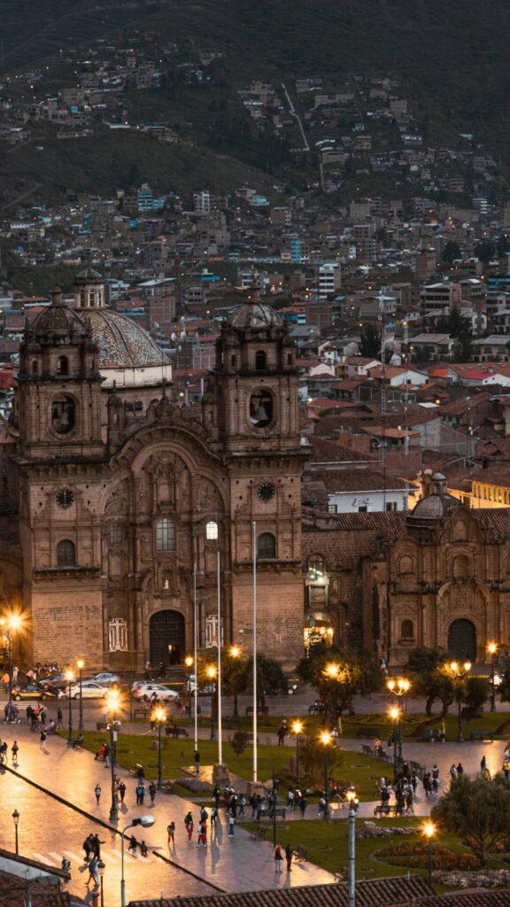 Una vista vertical de la Catedral de Cusco iluminada por la noche, con vistas a las luces de la ciudad y al centro histórico.