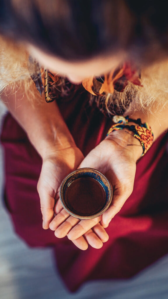 Vista superior de las manos de una persona sosteniendo un cuenco de madera lleno de medicina Ayahuasca durante una ceremonia en el Amazonas.