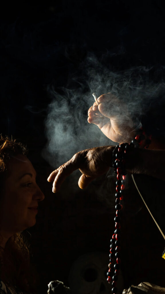 La mano de un chamán realizando un ritual de limpieza con humo sobre un participante en un entorno oscuro y místico.