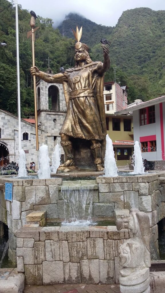 Una alta estatua dorada del emperador inca Pachacútec situada en el centro de una fuente en la plaza principal de Aguas Calientes.